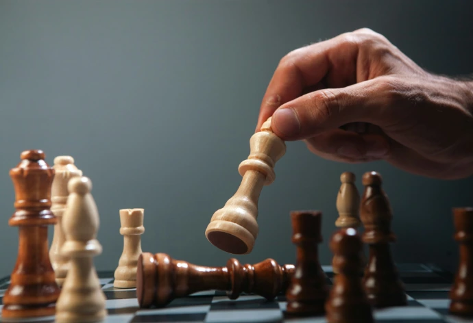 Hand moving a white chess piece over fallen king.